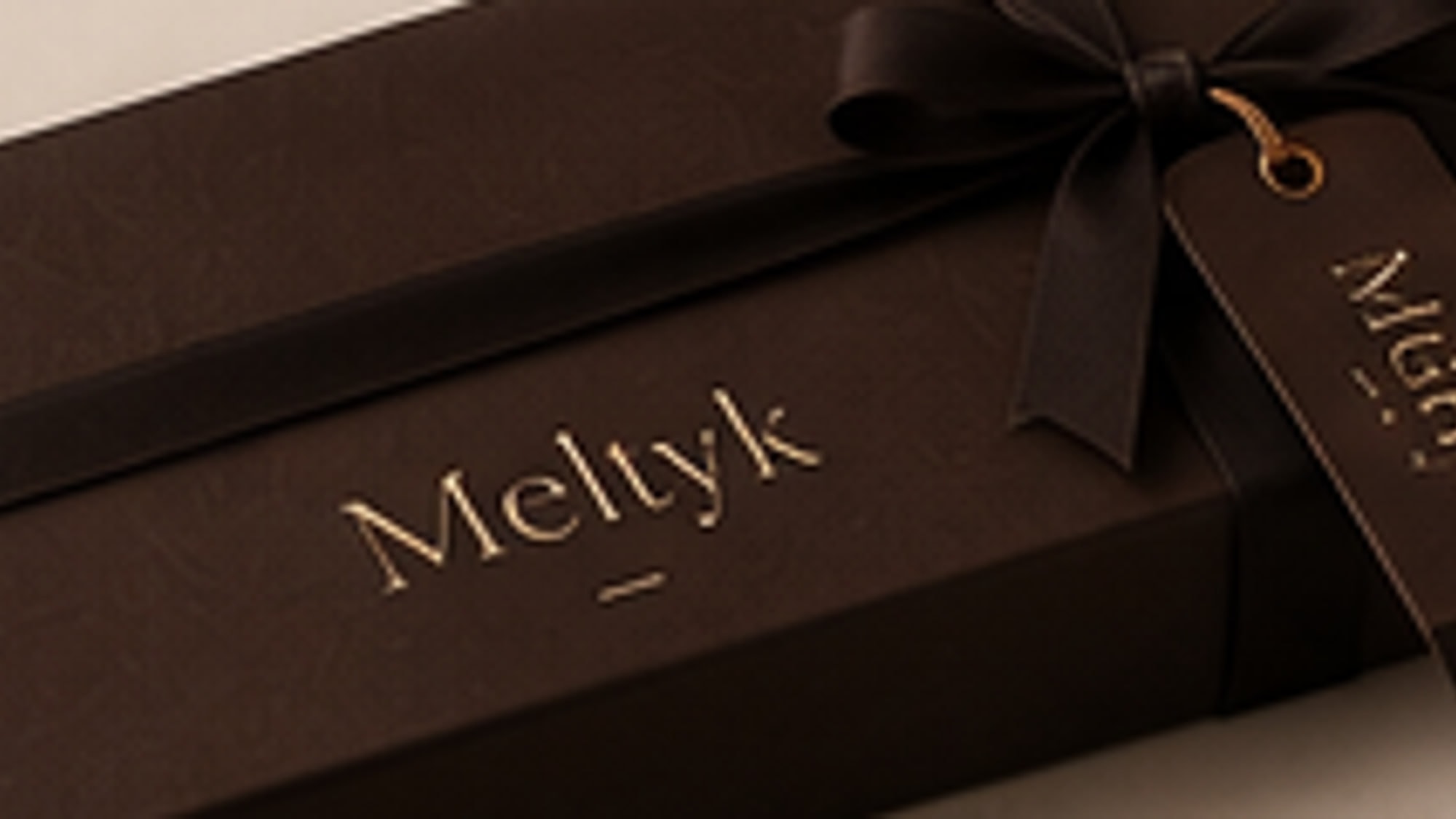 A Meltyk box tied with satin ribbon and a foil-blocked hang tag